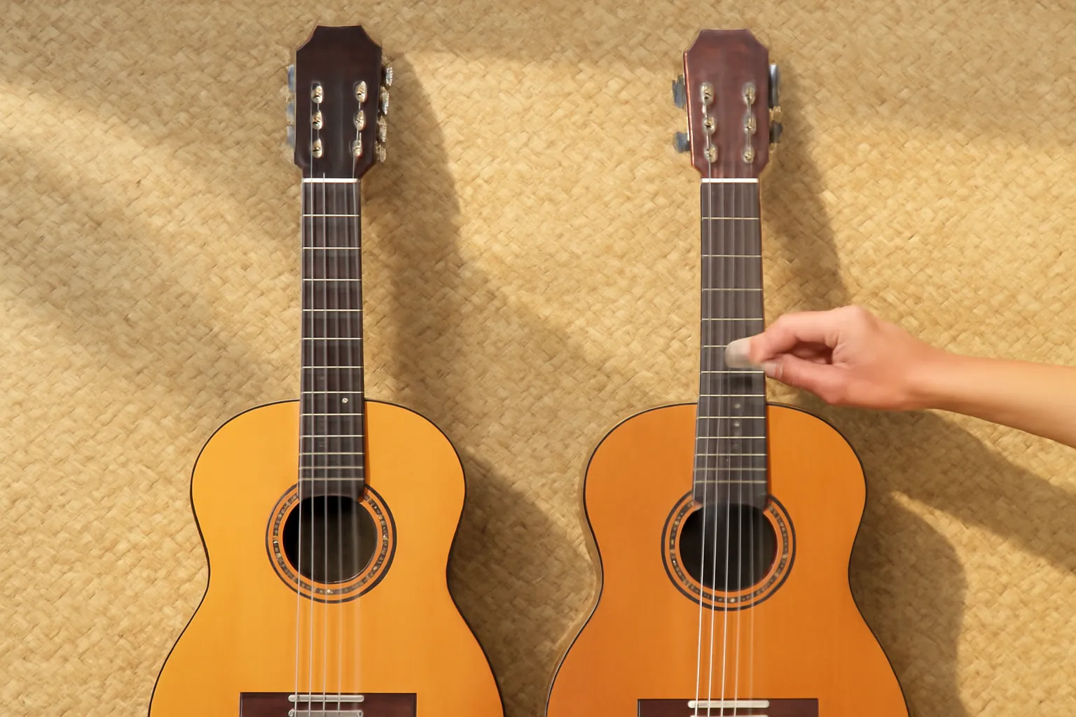 Hai cây guitar mặt gỗ nằm trên thảm cói, bàn tay vuốt dây